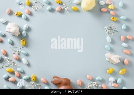 Easter border with pastel chocolate eggs, bunny, spring blossom flowers, and yellow chick on blue background. Top view. Flat lay. Happy Easter greetin Stock Photo