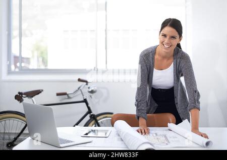 These plans are coming along nicely. Smiling young designer standing at her desk. Stock Photo