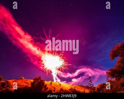 Bright red fireworks over a hill in a natural landscape at night against a starry sky, a rural holiday landscape Stock Photo
