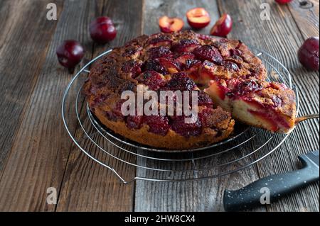 Plum cake baked upside down and served with cake server on a cooling rack isolated on dark wooden table Stock Photo
