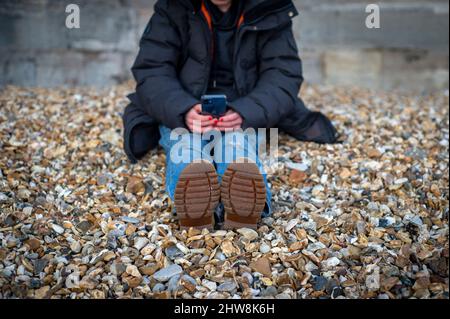 Close up of the soles of a pair of boots. Woman sitting relaxing looking at her phone. Stock Photo