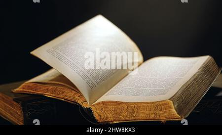 Open old book lying on the table with pages turning by wind. Vintage books, close-up. Stock Photo