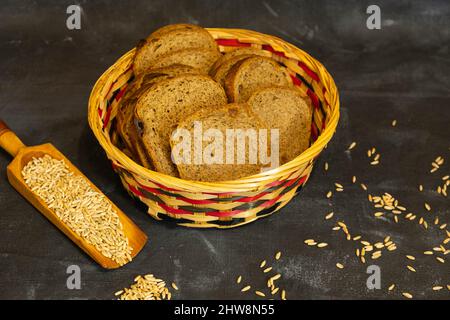 Sliced rye bread in a wicker basket. Scattered grain on a dark background. Stock Photo