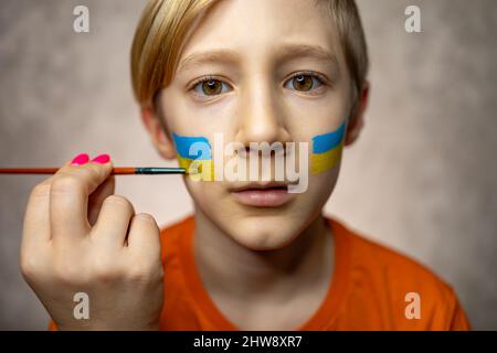 child against war, portrait of a boy with a painted flag of Ukraine on his cheeks Stock Photo
