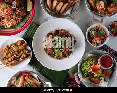 selective choice food table Shell Crab noodle , Chicken Satay, Spring Roll, Curry Samosa, fish cake, Folks Drumlet, Pork Jar Salad in a dish isolated Stock Photo