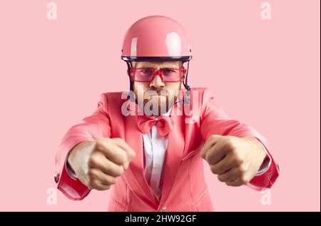Funny man in pink suit and helmet driving invisible car with angry face expression Stock Photo