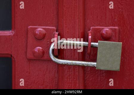 Old rural storage building Crimson red metal door with a padlock in Nafplio, Greece. Stock Photo