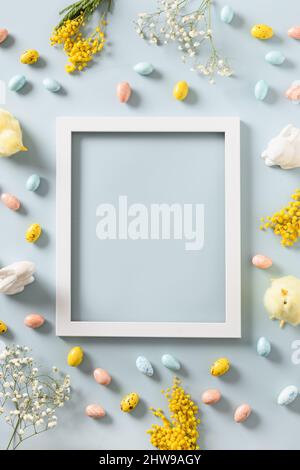 Easter frame and mock up with pastel chocolate eggs, flowers, bunny on blue background. Space for text. View from above. Flat lay. Vertical greeting c Stock Photo