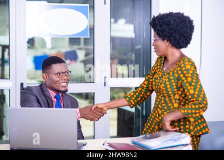 handsome businessman in jacket sitting at the desk greeting his colleague while smiling. Stock Photo