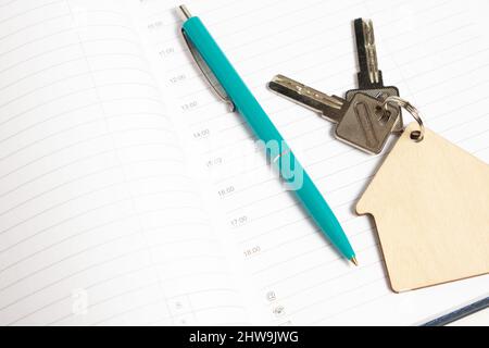 Keychain shape house with keys and ballpoint pen on an open notebook Stock Photo