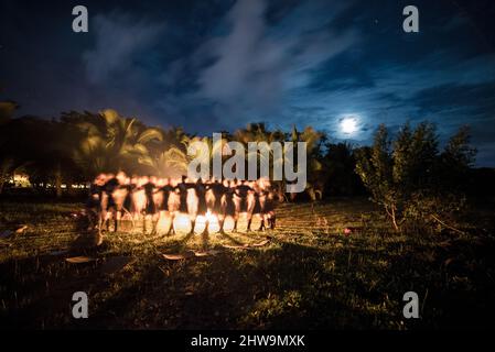 A beautiful shot of people dancing around a campfire, under the moonlight, in a tropical forest Stock Photo