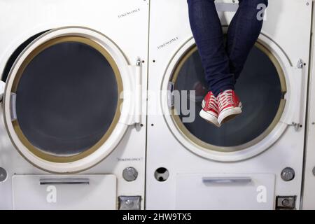 Relaxed at the laundromat. Cropped image a mans legs as he sits on a washing machine at the laundromat. Stock Photo