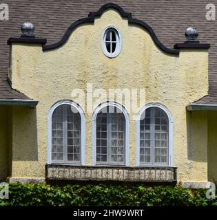 Yellow tinted stucco window framing has arched and circle windows.  Small decorative balcony sits under windows. Stock Photo