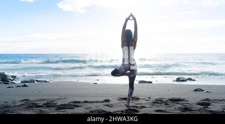 woman in sport clothes practicing yoga and meditating on beach in morning Stock Photo