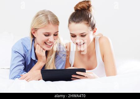 Hes cute isnt he - Social Networking. Two friends lying in bed using a digital tablet together. Stock Photo