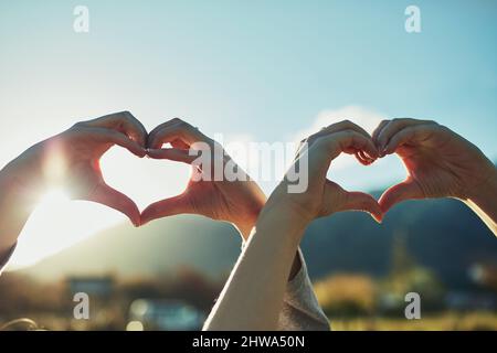 Loving life. Shot of two unrecognisable people making heart shapes with their hands outdoors. Stock Photo
