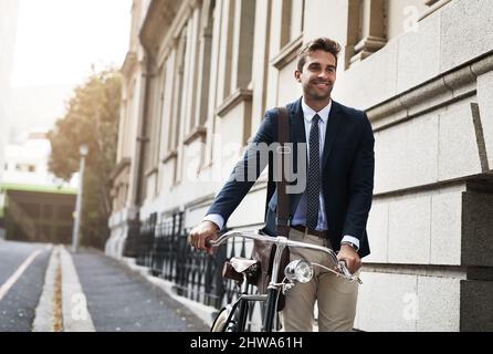 Time to get to work. Shot of a handsome young businessman pushing his bicycle while making his way to work in the morning. Stock Photo
