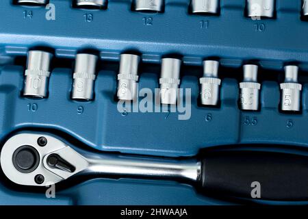 Top view of ratchet wrench and some stainless steel hex sockets on blue background. Stock Photo
