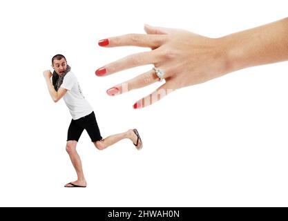Fear of commitment. A young man trying to run away from a giant hand wearing a wedding ring. Stock Photo