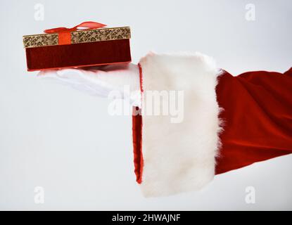 Saving the best for last. Cropped image of Santa holding a single present, with bow, in his white gloved hand. Stock Photo