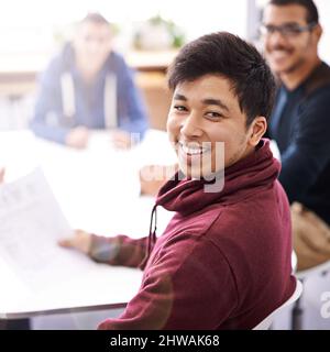 Meetings keep us on the same page. Portrait of a happy young man sitting in a meeting with his colleagues. Stock Photo