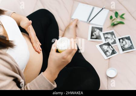 A pregnancy, people and maternity concept - close up of pregnant woman applying stretch mark cream to belly Stock Photo