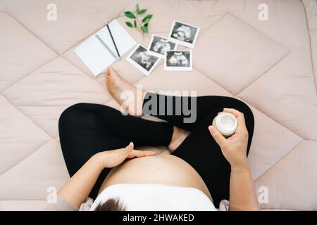 A pregnancy, people and maternity concept - close up of pregnant woman applying stretch mark cream to belly Stock Photo