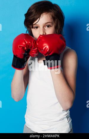 Training for the next big fight. Portrait of a young boy wearing boxing gloves in the studio.