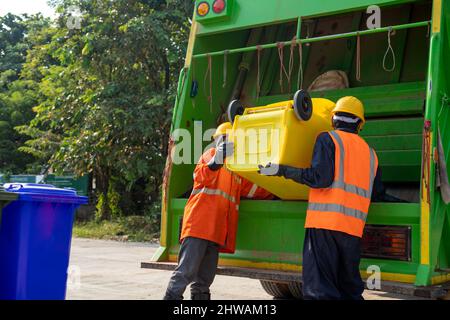 Garbage collector, Two garbage men working together on emptying dustbins for trash removal with truck loading waste and trash bin. Stock Photo