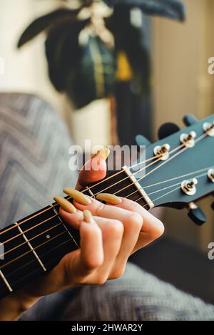 Girl plays guitar. Woman's hand with long nails clamps strings on guitar fretboard. Close-up. Stock Photo