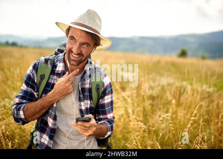 Hipster guy on the nature listens to music.happy man with backpack and smartphone outdoors