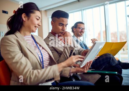 Young participants at a business lecture in a pleasant atmosphere in the conference room are reading writings together. Business, people, company Stock Photo