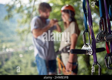 Selective focus on protection gear with blurred background of couple. Young attractive couple in casual clothing preparing for zip line adventure in f Stock Photo