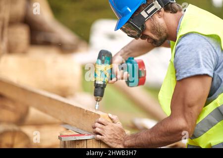 Close-up of handsome male builder working with tools at the construction site in the forest on a beautiful day. Construction, building, workers Stock Photo