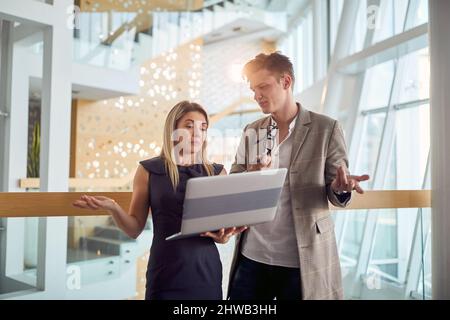 Two young business colleagues having a conversation about laptop content they watching together in a pleasant atmosphere in the hallway. Business, peo Stock Photo