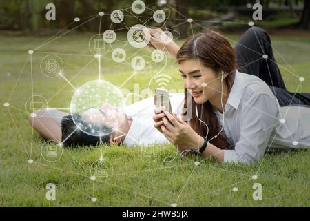 Happy asian couple using and listening the song and using the social network via smart mobile phone for online shopping with omni channel in the park, Stock Photo