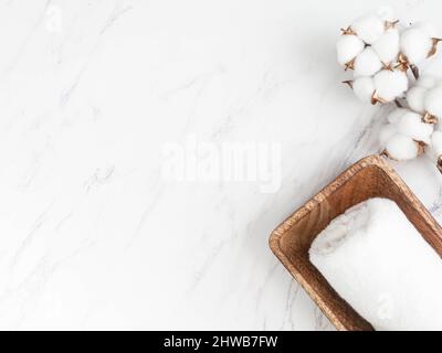 Minimal spa background or decor composition for advertising, cover. Cotton towels on wood tray and cotton branch on white marble background. Flat lay. Stock Photo