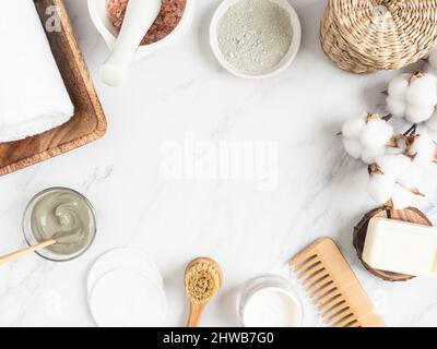 Home skin care concept. Organic blue clay for facial cosmetic mask, cotton pad, soap, candle, cream, cotton towel and sea salt in mortar on marble bac Stock Photo