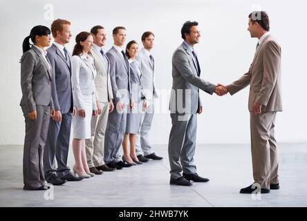 Welcome to the company. A young businessman welcoming a new employee to the company as colleagues look on. Stock Photo