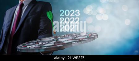 Target and goal in new year 2022 and 2023, business man holding dart board target with dart on center of target, success and plan to achievement in ma Stock Photo