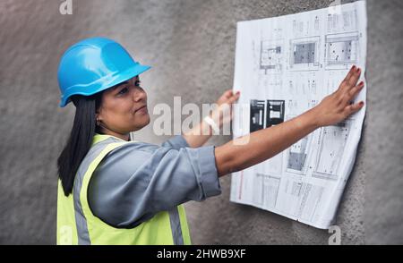 Taking another look at the blueprints. Cropped shot of an attractive young female construction worker working on site. Stock Photo