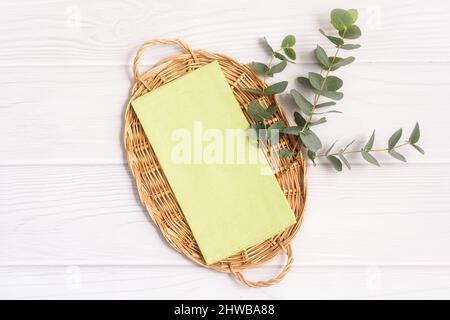 Green tea towel and twig of Eucalyptus on wicker tray on white wood table Stock Photo