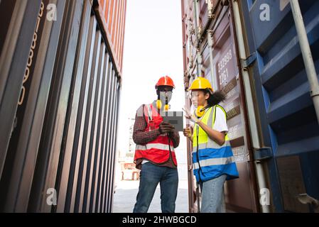 Two African american male and female worker using tablet and checking control loading freight containers from Cargo freight ship for import export. Stock Photo