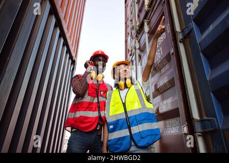 Two African american male and female worker using radio communication and checking control loading freight containers from Cargo freight ship for impo Stock Photo