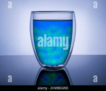 Double-walled insulated glass beaker, filled with blue and green liquid and round ice.Bright reflective background Stock Photo