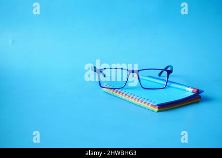notepad, eyeglass and a pencil on blue color background  Stock Photo