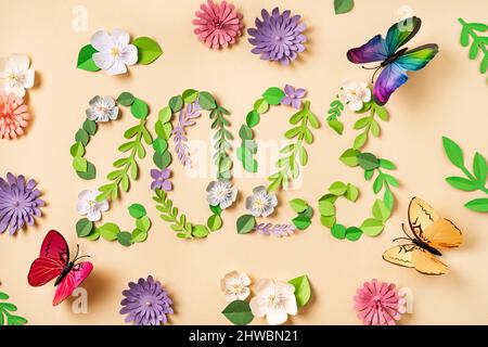 2023 number made from paper flowers and leaves. Beautiful butterflies fly around. Paper art design. Floral natural background Stock Photo