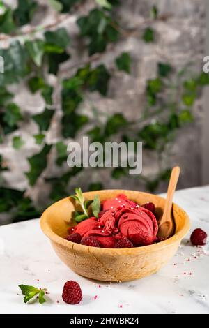 Delicious and refreshing raspberry sorbet in rustic wooden bowl on the table in the garden or balcony Stock Photo