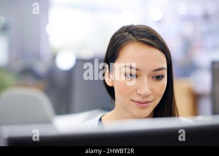 Focussing on her work with a positive spirit. Shot of an attractive young woman sitting at her workstation in the office. Stock Photo