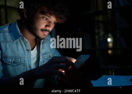 Young indian man using mobile apps on cell phone late at night. Stock Photo